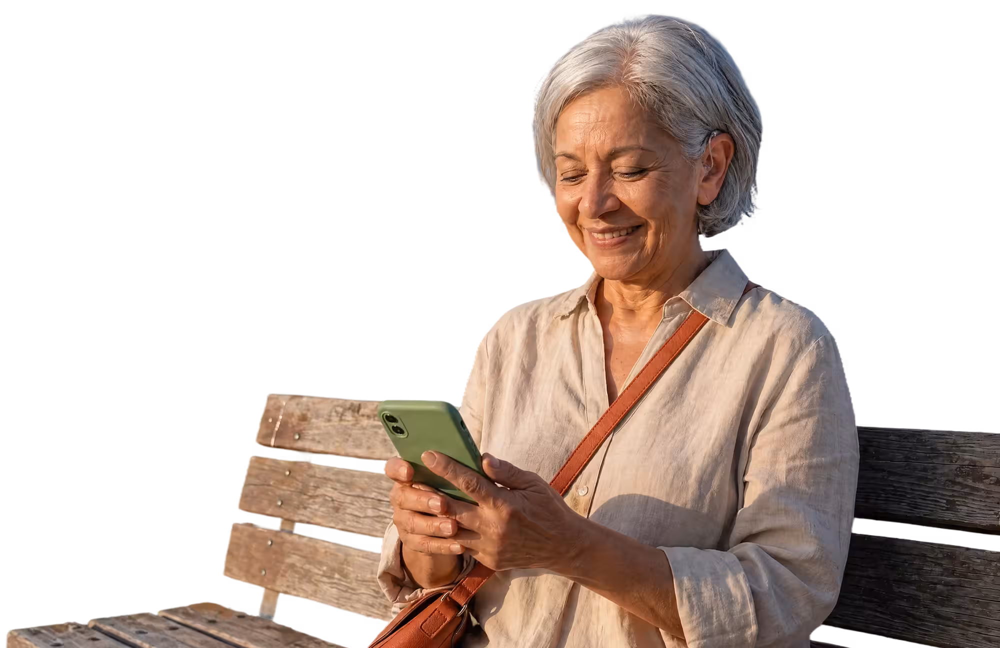Smiling older woman with short gray hair and a hearing aid, sitting on a wooden bench and looking at a green smartphone.