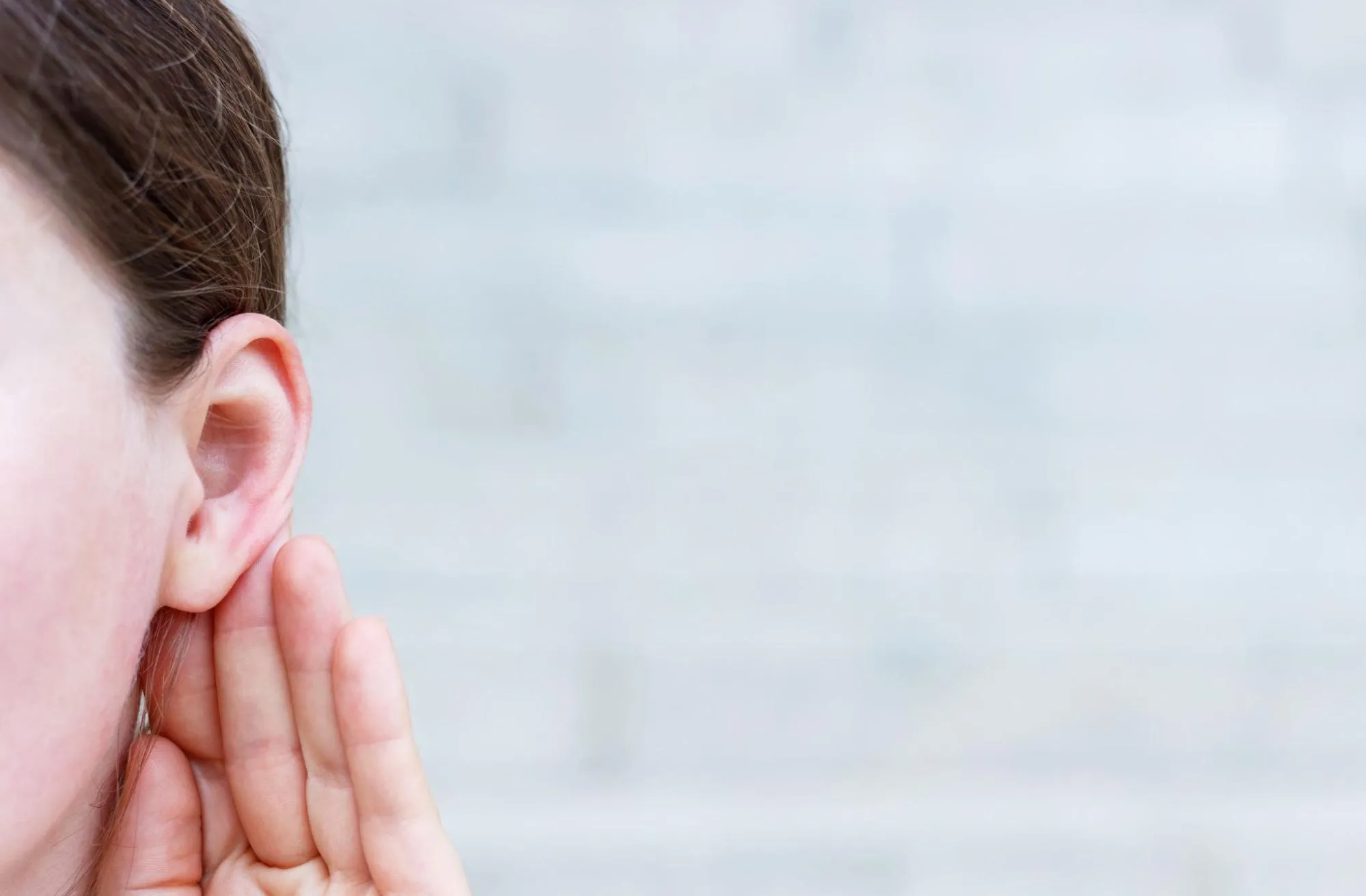 A person leaning in to listen, a hand cupped behind one ear.